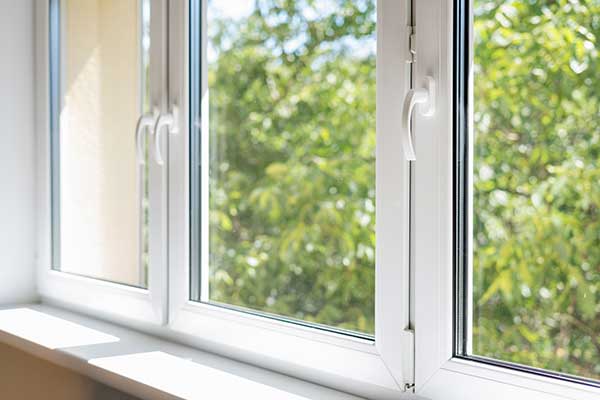 White-frame windows with handles that open up to a view of trees outside