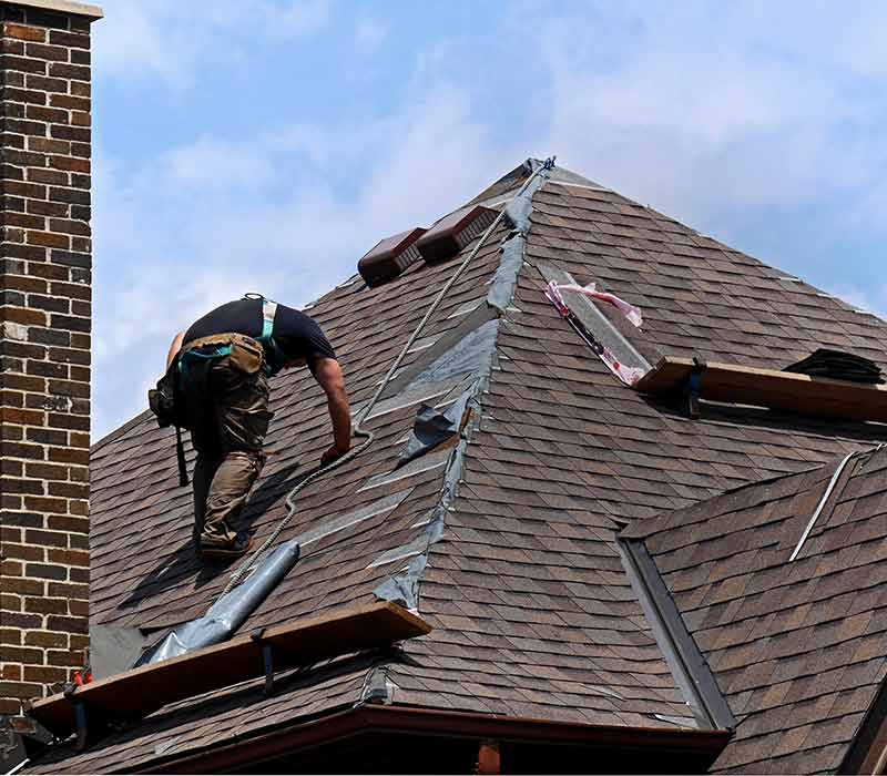 Worker on a sloped residential roof installing new brown shingles
